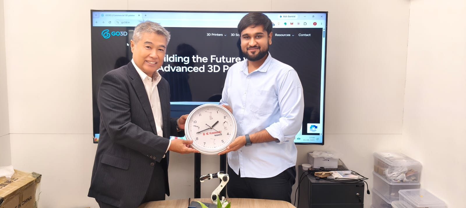Kawasaki Robotics India and Go3D teams hold a Kawasaki Robotics clock at the Go3D office in Ahmedabad, with the go3d.in website on the screen behind them